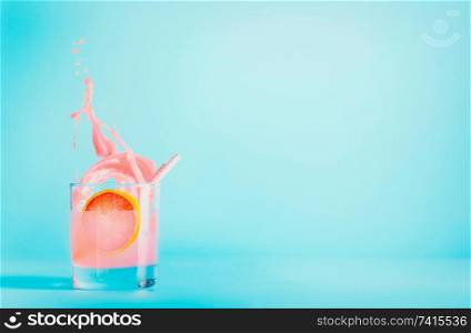 Grapefruit drink in glass with splash on blue background. Summer refreshing beverage . Pink grapefruit lemonade . Copy space