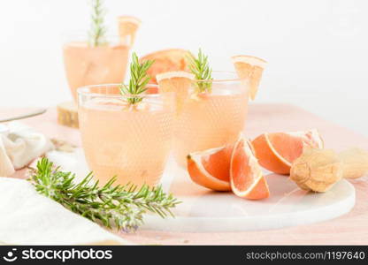 Grapefruit juice with rosemary in glasses on the table. Refreshing summer cocktail.