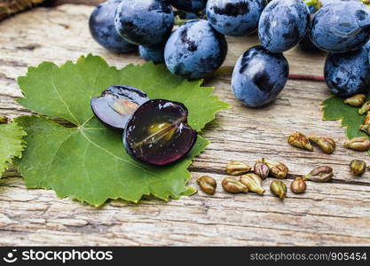 Grapes and grape seeds on a green leaf on old wooden boards. Blue grape. Spa, bio, eco products concept.. Grapes and grape seeds on a green leaf on old wooden boards. Blue grape. Spa, eco products concept.