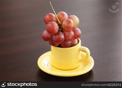 grapes in a cup and saucer on a wooden table