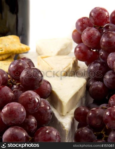 Grapes in the foreground, and cheese and a bottle of wine in the background