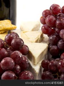 Grapes in the foreground, and cheese and a bottle of wine in the background