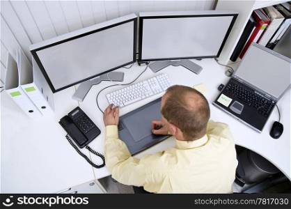 Graphic designer at work behind two big flatscreen monitors and a laptop A clipping path of the screens is available at the highest resolution