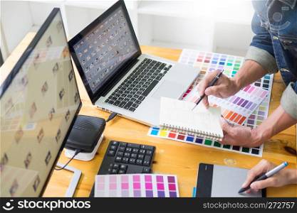 graphic designer team working on web design using color swatches editing artwork using tablet and a stylus At Desks In Busy Creative Office
