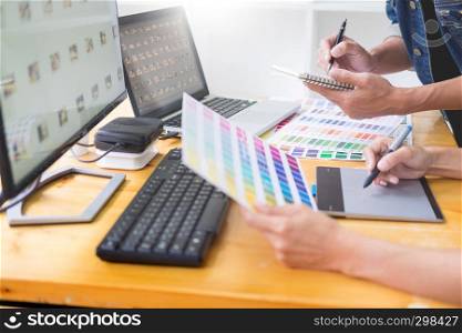 graphic designer team working on web design using color swatches editing artwork using tablet and a stylus At Desks In Busy Creative Office