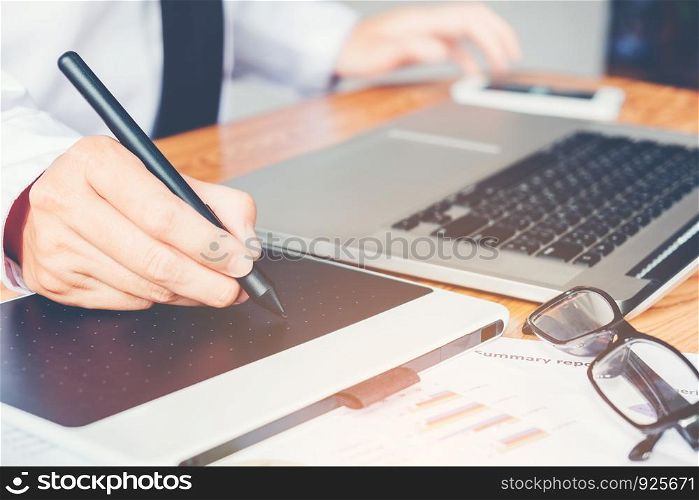 graphic designer working and writing on graphic tablet while using laptop