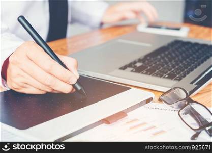 graphic designer working and writing on graphic tablet while using laptop
