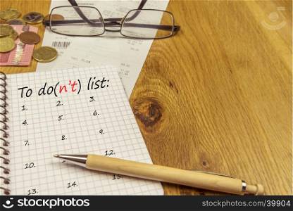 Graphic notebook with a to do list, placed on a wooden office desk, surrounded by bills, money and a pair of glasses