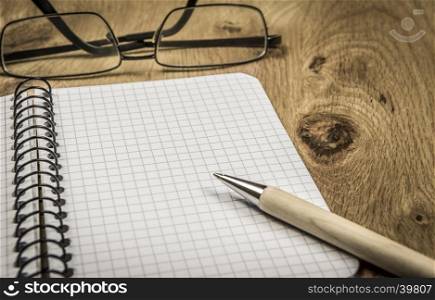 Graphic spiral notebook with copy space and eyeglasses on wooden desk, in vintage settings