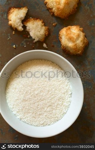 Grated coconut in bowl with coconut macaroons on slate, photographed overhead with natural light (Selective Focus, Focus on the grated coconut)
