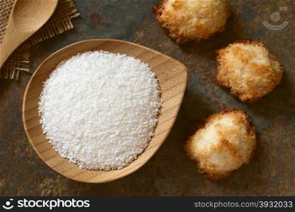 Grated coconut on small plate with coconut macaroons on slate, photographed overhead with natural light (Selective Focus, Focus on the grated coconut and the top of the macaroons)
