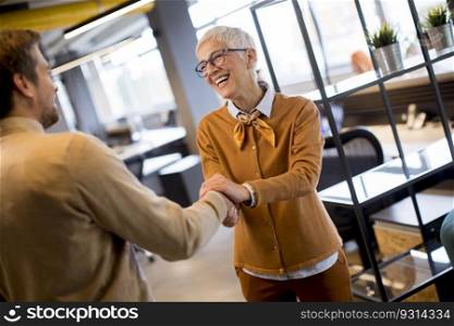 Grateful senior  businesswoman  boss lady hold hand of best employee,  shake hands warm welcoming standing in coworking space