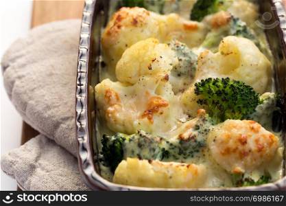 Gratin of cauliflower, broccoli and cheese in brown rustic dish.