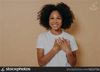 Gratitude concept. Happy thankful young african woman isolated on yellow studio background holding hands on chest and feeling gratful, smiling dark skinned lady showing appreciation and love. Thankful young african woman isolated on yellow studio background showing appreciation and love