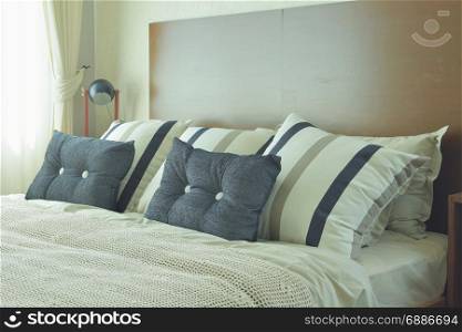Gray and brown strip pillows setting on white linen bedding with brown wooden headboard