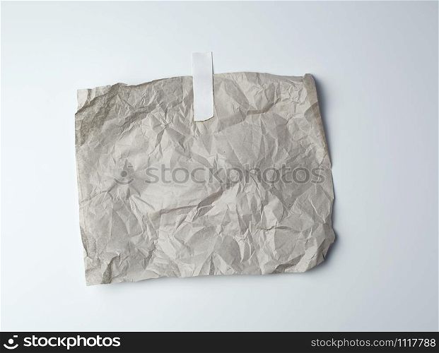 gray crumpled sheet of paper glued with white adhesive tape on a white background, place for text