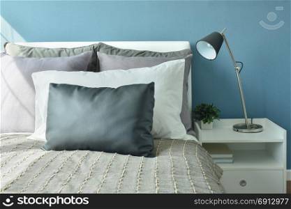 Gray, dark gray and white color pillows on bed with modern style table lamp