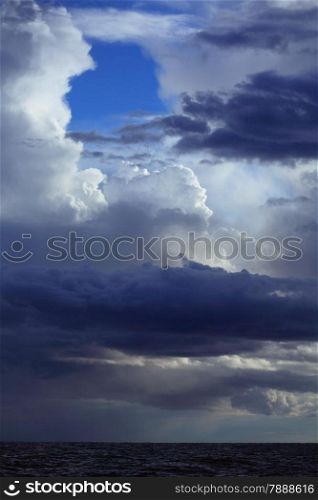 Gray deep blue fluffy thunder clouds stormy sky above a dark surface of the sea. Meteorology