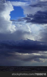 Gray deep blue fluffy thunder clouds stormy sky above a dark surface of the sea. Meteorology