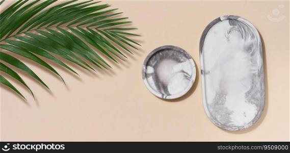 Gray empty decorative plate and green palm leaf on a beige background, product and cosmetic display stage, top view
