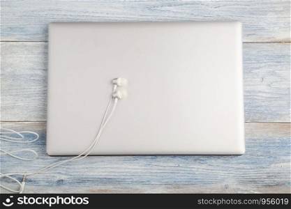 gray laptop with white headphones on a light blue old wooden background. top view. flat lay