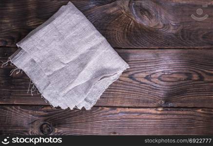 gray linen napkin on a brown wooden background, empty space on the right
