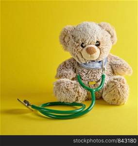 gray teddy bear and green medical stethoscope on a yellow background, treatment concept for children