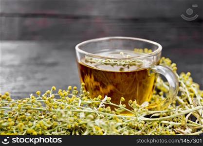 Gray wormwood herbal tea in a glass cup, fresh sagebrush flowers on wooden board background