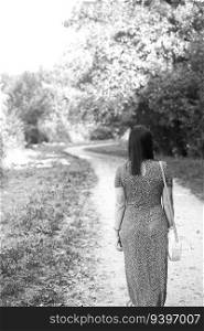 Grayscale photo of a woman walking by a path through the forest