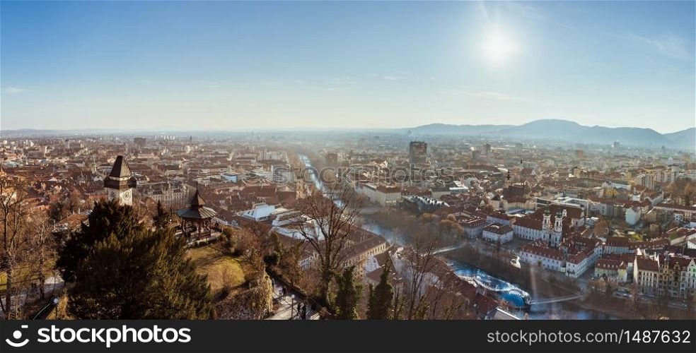 Graz, Styria Austria - 20.01.2019: Wide panorama of Graz City, City rooftops, Mur river and city center, Schlossberg hill and clock tower Sun in winter, blue sky. Travel destination.. Wide panorama of Graz City from castle hill Schlossberg, Travel destination.