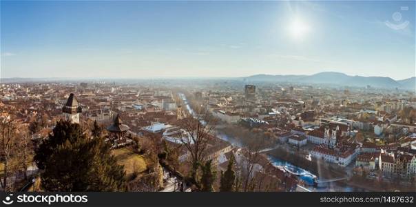 Graz, Styria Austria - 20.01.2019: Wide panorama of Graz City, City rooftops, Mur river and city center, Schlossberg hill and clock tower Sun in winter, blue sky. Travel destination.. Wide panorama of Graz City from castle hill Schlossberg, Travel destination.
