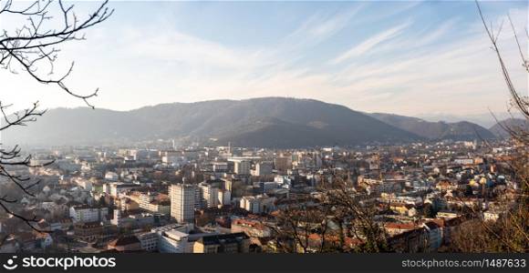 Graz, Styria Austria - 20.01.2019: Wide panorama of Graz City, City rooftops, residential area, mountains in background Sun in winter, blue sky. Travel destination.. Wide panorama of Graz City from castle hill Schlossberg, Travel destination.