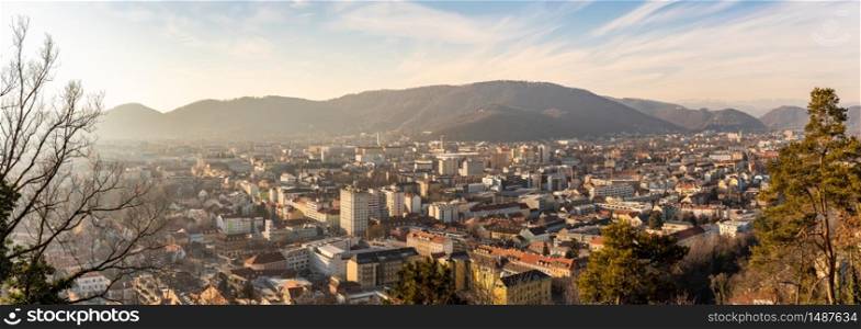 Graz, Styria Austria - 20.01.2019: Wide panorama of Graz City, City rooftops, residential area, mountains in background Sun in winter, blue sky. Travel destination.. Wide panorama of Graz City from castle hill Schlossberg, Travel destination.