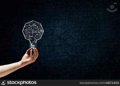 Great bright idea in darkness. Male hand on dark background showing drawn light bulb