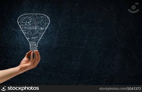 Great bright idea in darkness. Male hand on dark background showing drawn light bulb