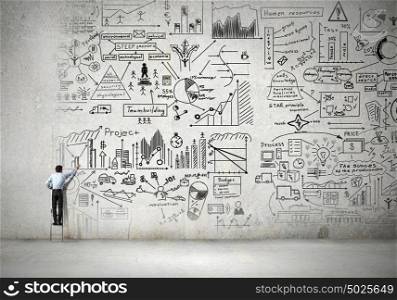 Great business strategy. Back view of businessman standing on ladder and drawing sketch on wall