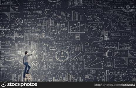 Great business strategy. Back view of man standing on ladder and drawing sketch on wall