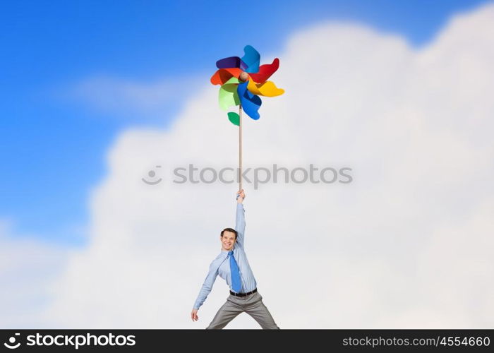 Great day for freedom. Young happy businessman flying in sky on colorful windmill