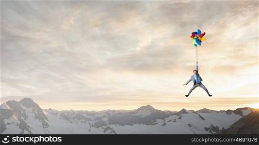 Great day for freedom. Young happy businessman flying in sky on colorful windmill
