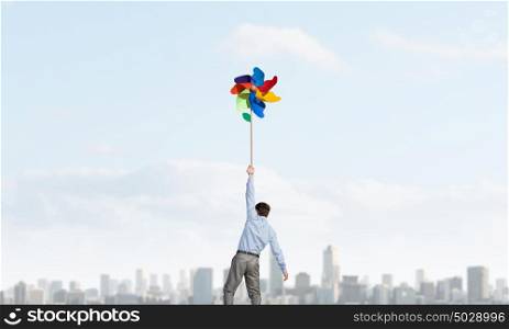 Great day for freedom. Young happy businessman flying in sky on colorful windmill