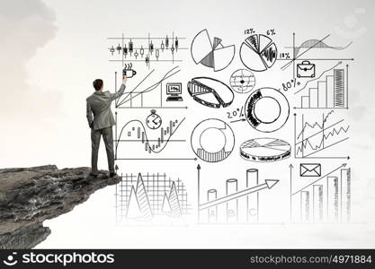 Great plan for reaching top. Back view image of businessman on rock top drawing business sketches