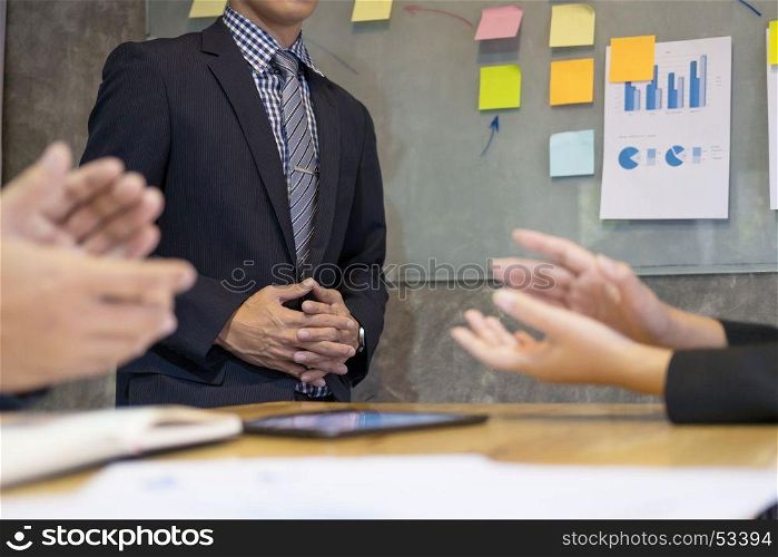 Great presentation! Group of business people in smart casual wear sitting together addressing applauding after speech of a businessman standing near whiteboard at the conference meeting around boardroom table.