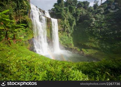 Great waterfall scenery with a rainbow. Tad Yuang, dramatic waterfall drops 40 metres over a cliff and tropical forest. Bolaven Plateau, Paksong, Laos. Rainy season.