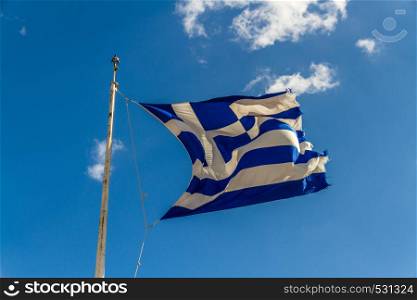Greek flag billowing against blue sky with some clouds