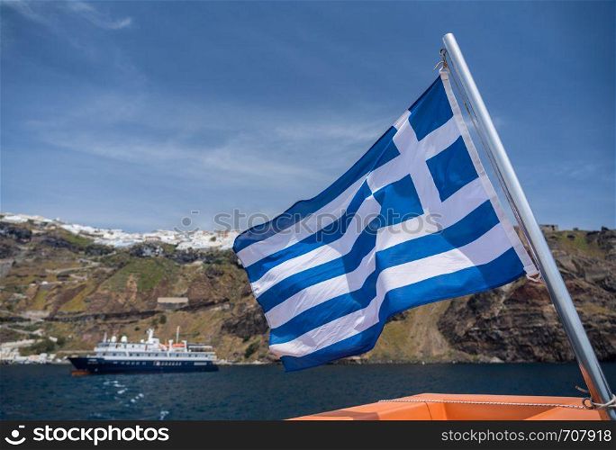 Greek flag on tender boat leaving Fira port on Santorini. Fira port on volcanic caldera island of Santorini