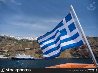 Greek flag on tender boat leaving Fira port on Santorini. Fira port on volcanic caldera island of Santorini