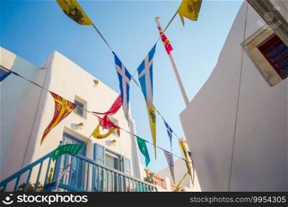 Greek flags on cyclades, traditional white house on background. Street with colorful flags in Mykonos, Greece