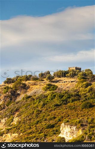 Greek idyllic hills with small shrubs of Mediterranean flora and little castle against cloudy sky.. Castle hills in greece during summer