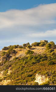 Greek idyllic hills with small shrubs of Mediterranean flora and little castle against cloudy sky.. Castle hills in greece during summer