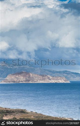 Greek island Monemvasia and cloudy sky, view from distance. Greece Peloponnese Lakonia. View of Monemvasia island in Greece